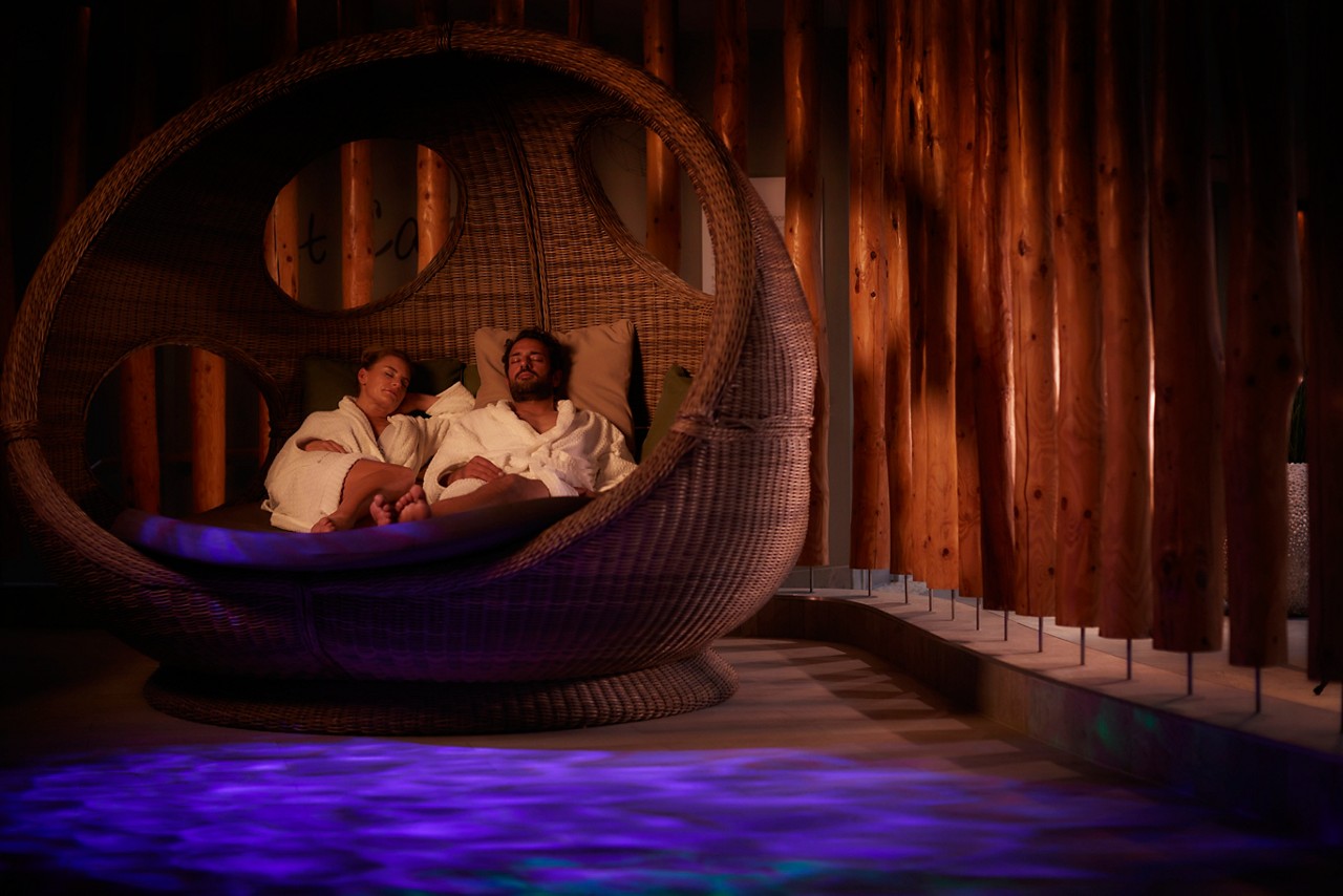 Couple snuggled in a large, cosy cocoon chair in the Forest Nesting area.